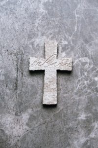 Stone cross with inscription Believe on grey background, Copy space. Christian backdrop. Biblical